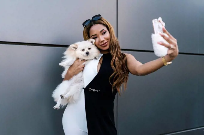 Young woman with dog taking selfie while standing in front of wall