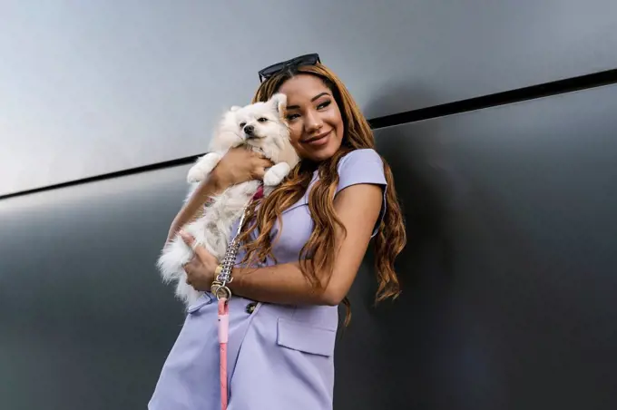 Young woman embracing dog while standing in front of gray wall