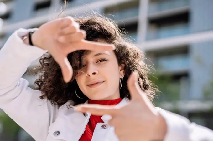 Young woman making finger frame with hands on sunny day