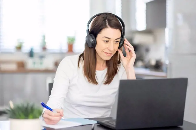 Smiling female entrepreneur wearing headphones working at home