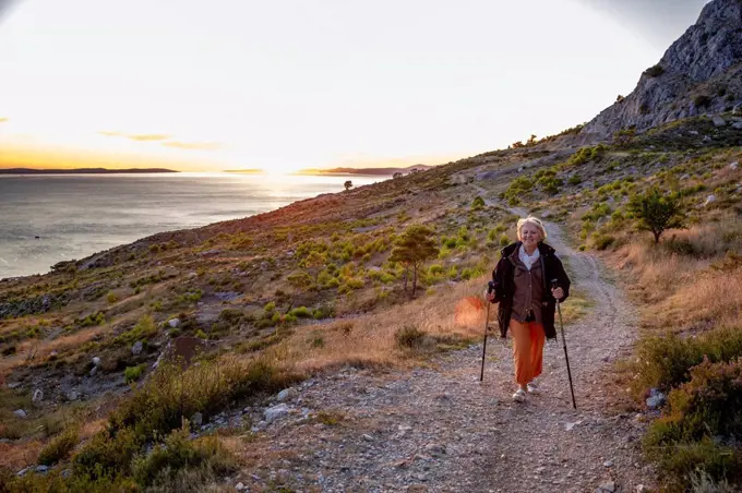 Senior woman with hiking poles on footpath near Adriatic sea in Omis, Dalmatia, Croatia