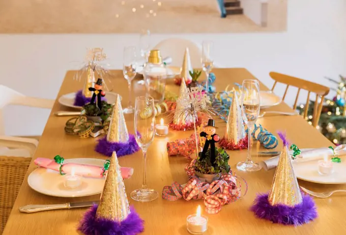 Festive laid New Years Eve table with plates, candles, party hats, champagne flutes and chimney sweep figurines