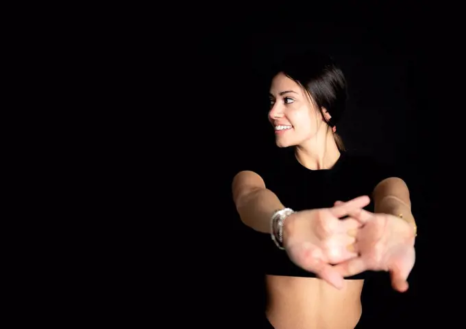 Smiling female athlete looking away while stretching in front of black background