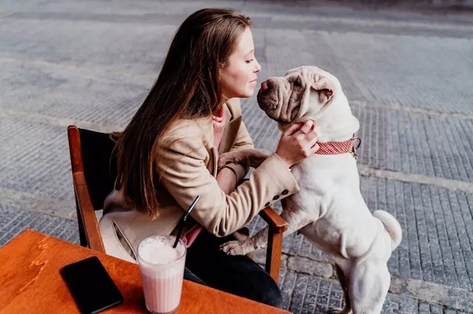 Woman looking at pet while sitting at sidewalk cafe