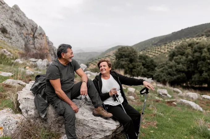 Senior couple hiking in the mountains smiling while sitting on rock