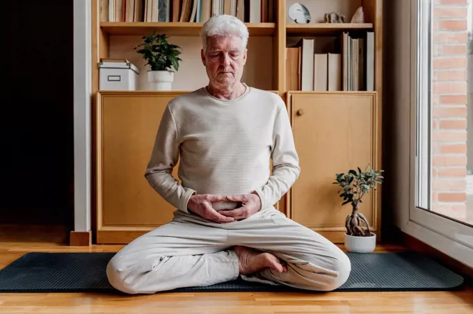 Senior man meditating while sitting with cross-legged at home