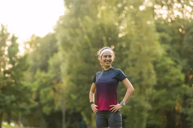 Smiling woman with hands on hip standing in public park