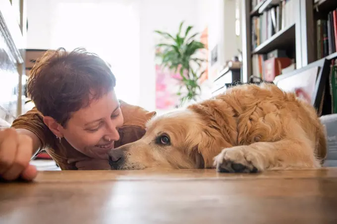 Smiling woman looking while lying with tired dog on parquet floor at home