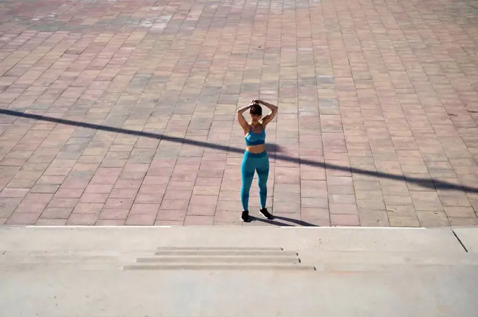 Female athlete tying hair in front of steps during sunny day