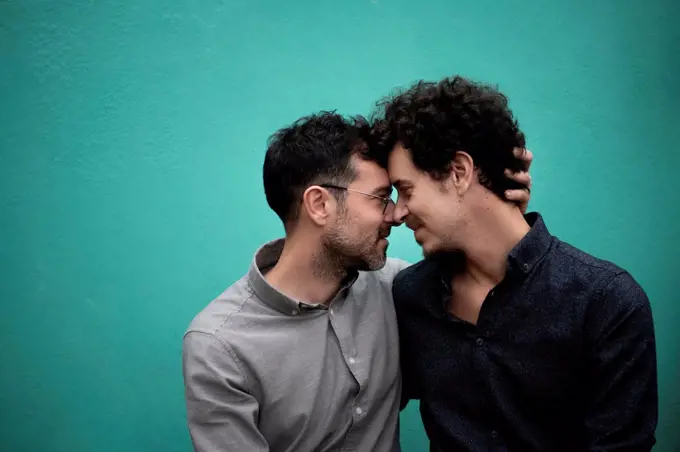 Gay couple romancing in front of Turquoise wall