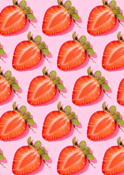 Pattern of rows of fresh halved strawberries lying against pink background