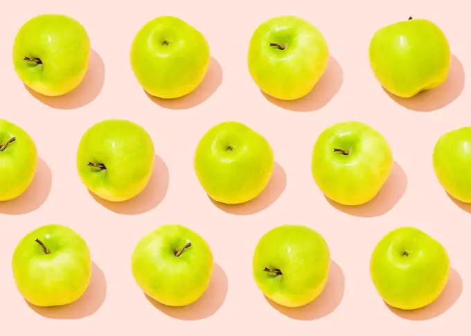 Pattern of green apples lying against light pink background