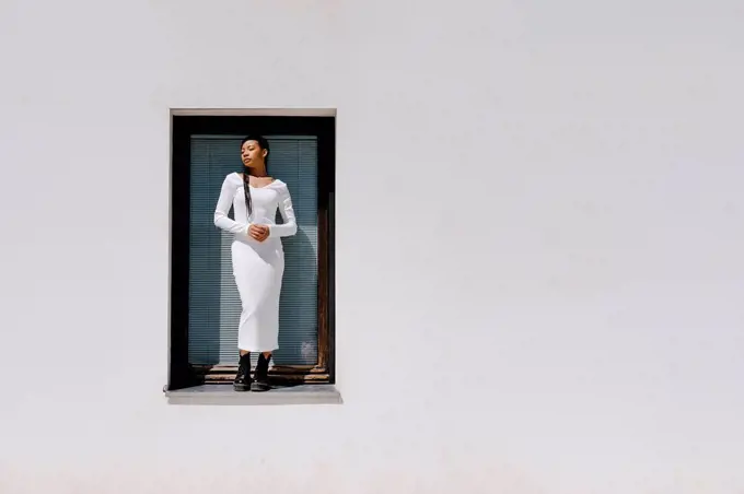 Woman with eyes closed standing on window sill