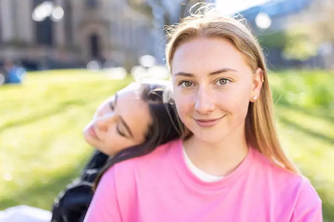 Beautiful blond woman with head on shoulder of female friend in public park