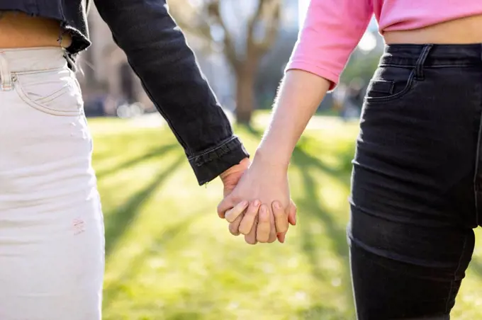 Female friends holding hands in public park