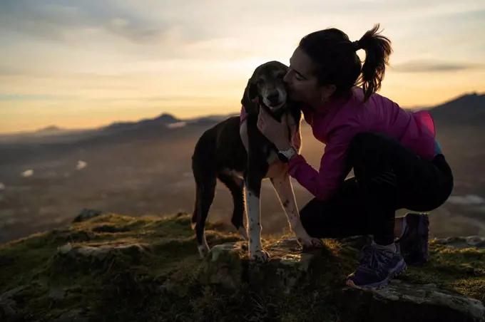 Woman kissing dog while kneeling on hill