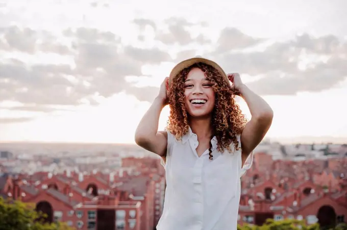 Cheerful woman smiling in front of city during sunset