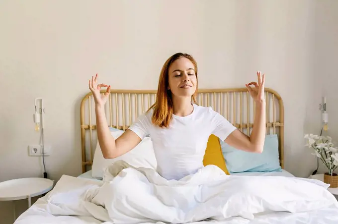 Redheaded woman meditating on bed at home