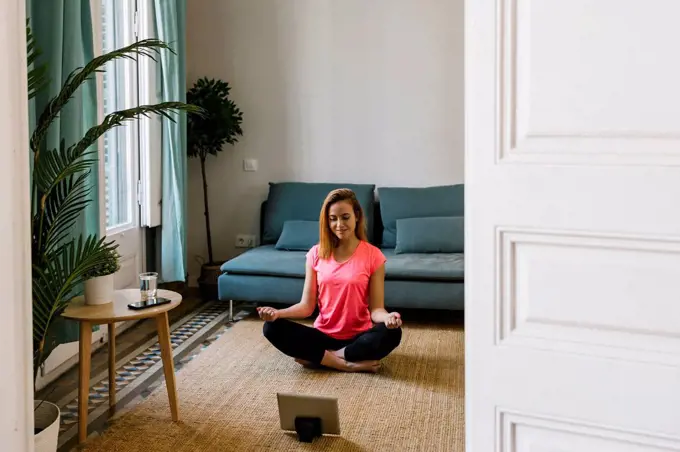 Young woman meditating in living room at home