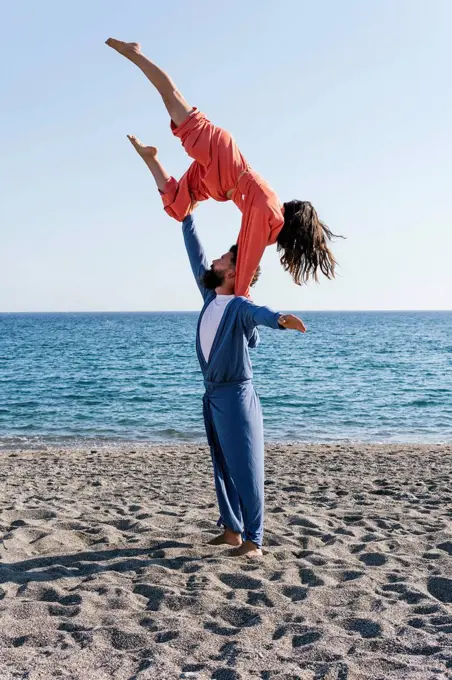 Girlfriend balancing on boyfriend shoulder while practicing acroyoga on beach