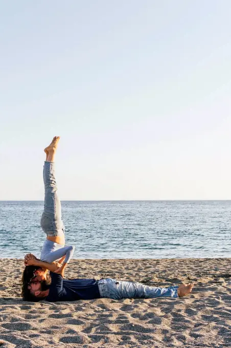 Couple kissing while practicing acroyoga on beach during sunny day
