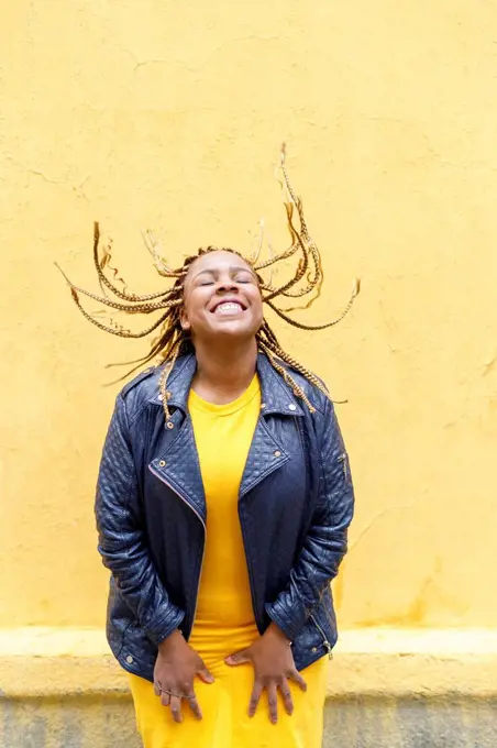 Playful plus size woman tossing braids in front of yellow wall