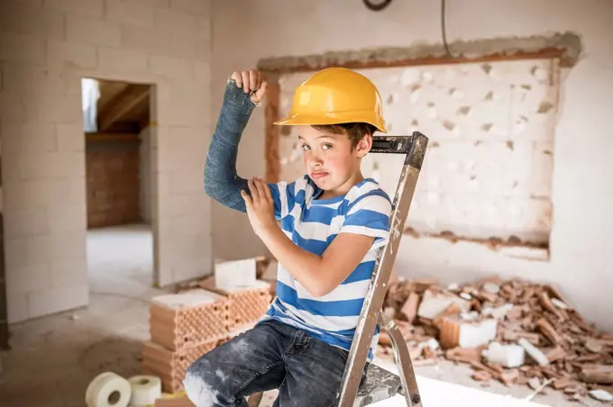 Boy flexing broken arm muscles while sitting on ladder during house renovation