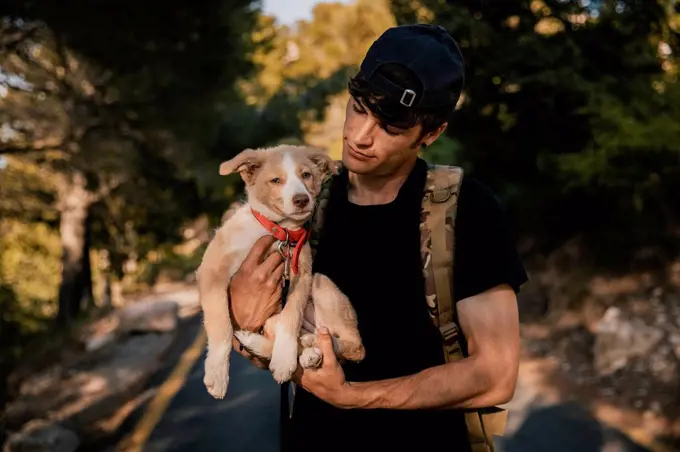 Young male hiker standing with backpack and pet in forest