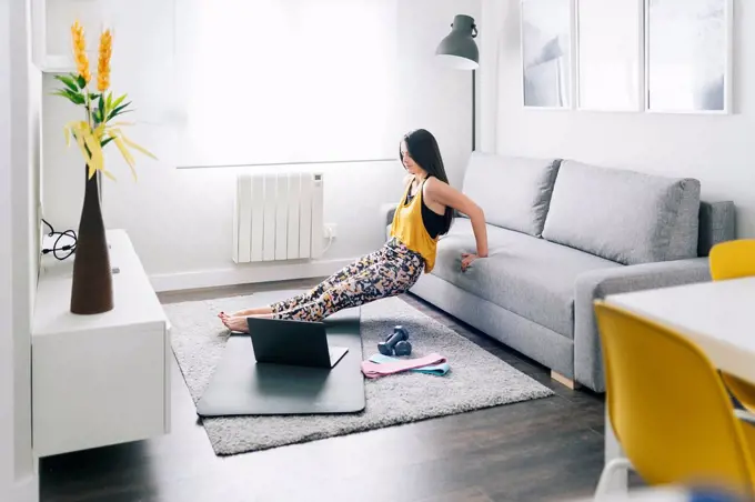Woman exercising while leaning on sofa by laptop at home
