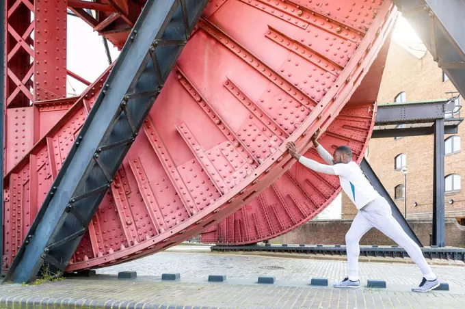 Young man stretching under red metallic structure at bridge