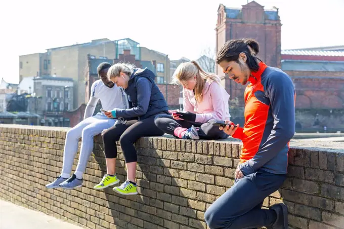 Multi-ethnic fitness friends using smart phones at wall