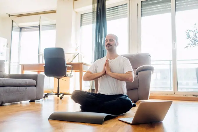 Man with hands clasped meditating while sitting on mat at home