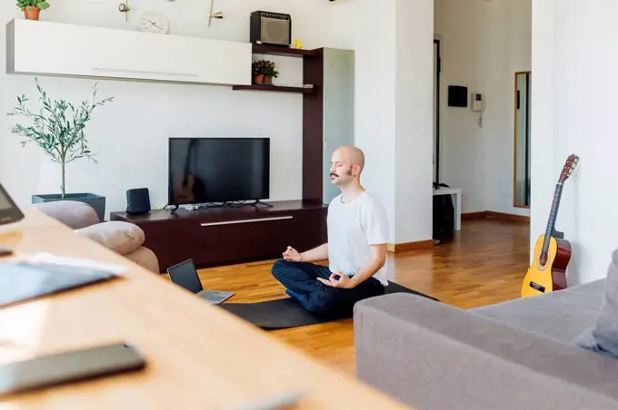Young man learning online yoga through laptop at home