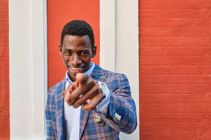 Young male entrepreneur smiling while pointing in front of wall