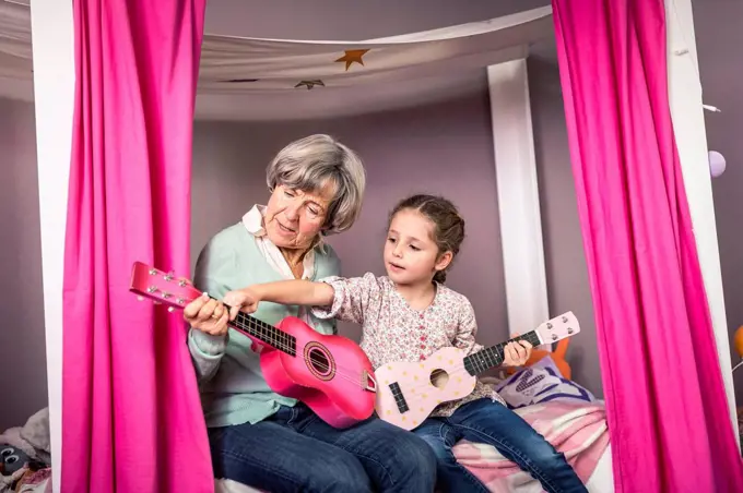 Granddaughter teaching about guitar to grandmother in bedroom