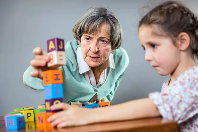 Senior woman stacking toy block while playing with girl at home
