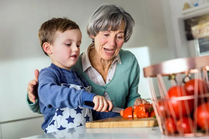 Grandson cutting tomato by grandmother in kitchen