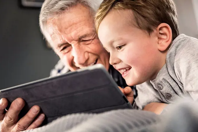 Smiling boy using digital tablet with senior man at home