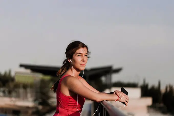 Sportswoman listening to music while leaning on railing