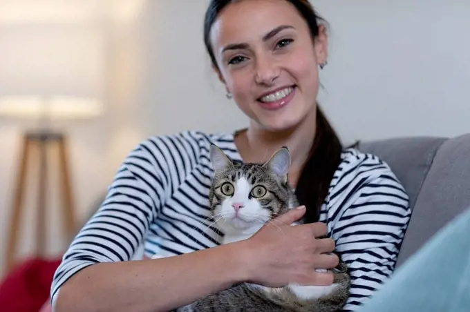 Smiling woman with tabby cat on sofa at home