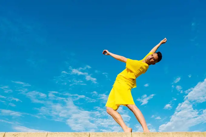 Young man dancing on retaining wall by blue sky