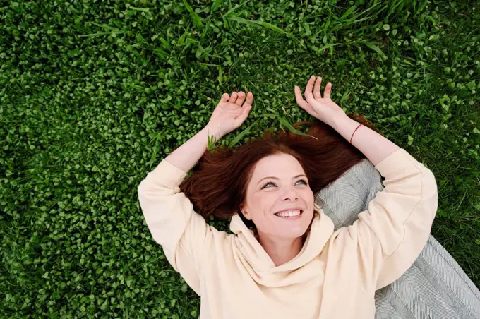 Happy mature woman lying on grass at public park