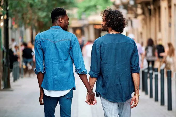 Gay couple holding hands looking at each other while walking on footpath