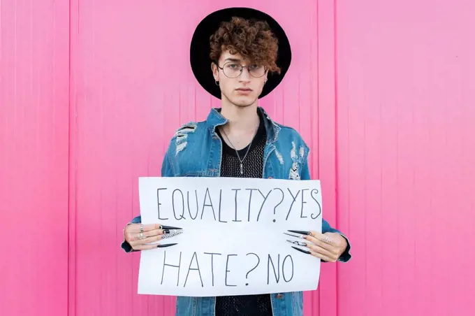 Serious gay man holding placard in front of pink wall