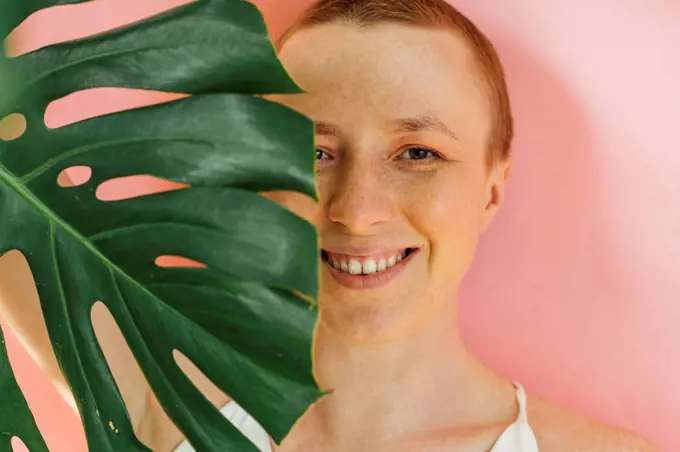 Smiling woman's half face covered with green leaf