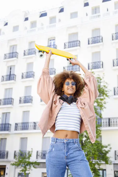 Cheerful young woman looking away while holding yellow skateboard