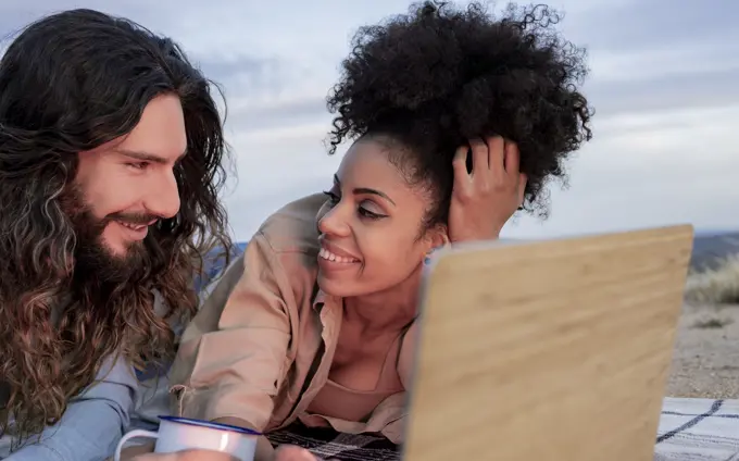 Smiling boyfriend looking at girlfriend lying by laptop