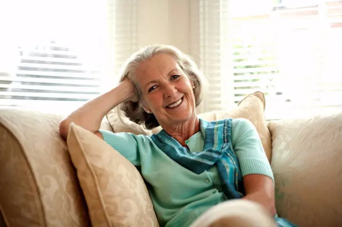 Smiling senior woman with head in hand sitting on sofa at home