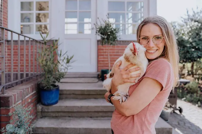 Smiling woman embracing chicken while standing in backyard