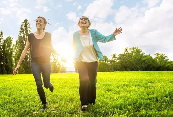 Happy women holding hands while running on meadow